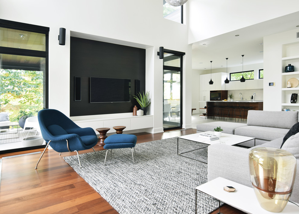 Exempel på ett modernt allrum med öppen planlösning, med vita väggar, mellanmörkt trägolv, en väggmonterad TV och brunt golv