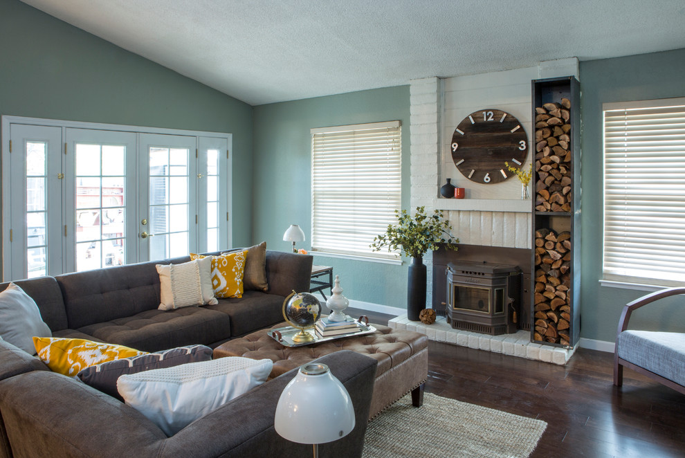 Aménagement d'un grand salon contemporain ouvert avec un mur bleu, parquet foncé, un poêle à bois et un manteau de cheminée en brique.