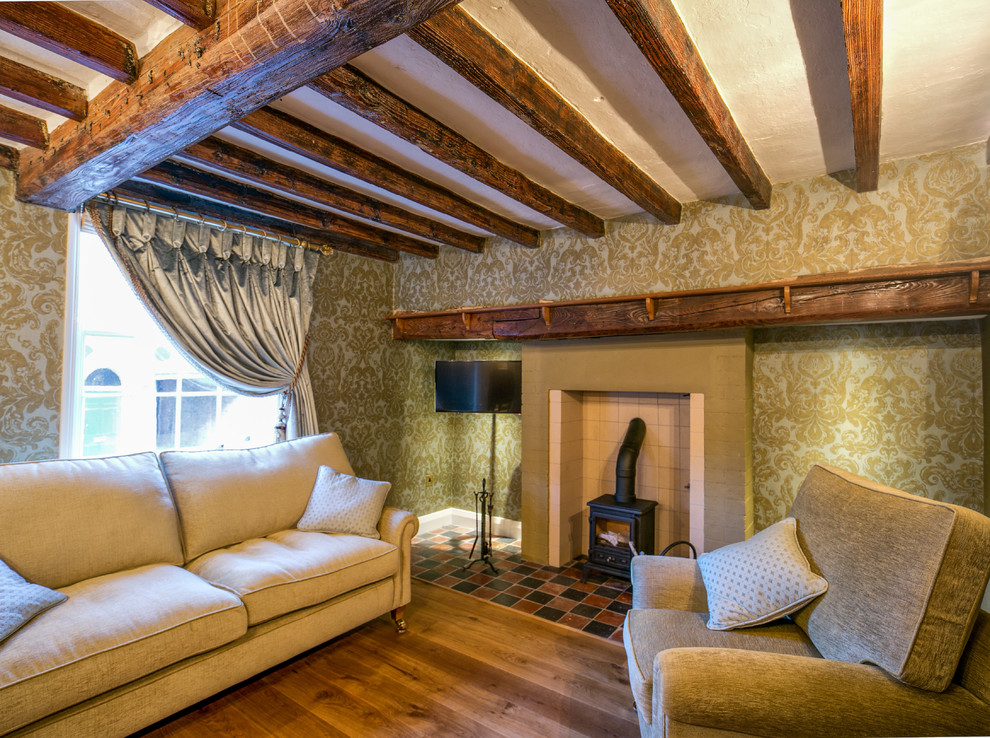 Immagine di un grande soggiorno country con pareti verdi, pavimento in legno massello medio, stufa a legna, cornice del camino in pietra e TV a parete
