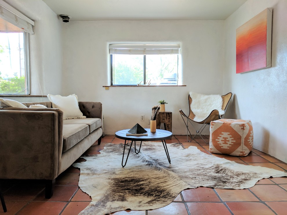 他の地域にある小さなサンタフェスタイルのおしゃれな独立型リビング (白い壁、テラコッタタイルの床、コーナー設置型暖炉、漆喰の暖炉まわり、テレビなし、オレンジの床) の写真