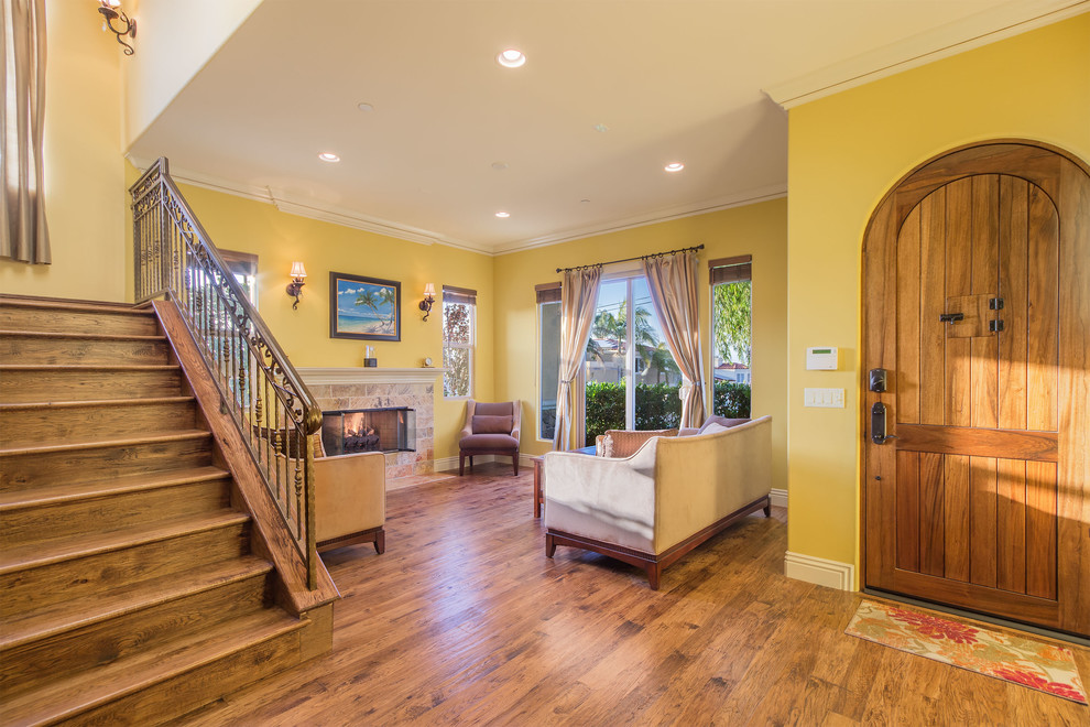 Kleines, Offenes Mediterranes Wohnzimmer mit gelber Wandfarbe, braunem Holzboden, Kamin und gefliester Kaminumrandung in Los Angeles
