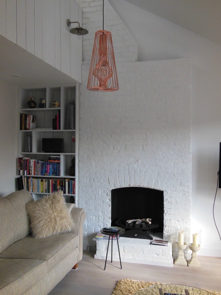 This is an example of a medium sized scandinavian open plan living room in London with a reading nook, white walls, light hardwood flooring and a brick fireplace surround.