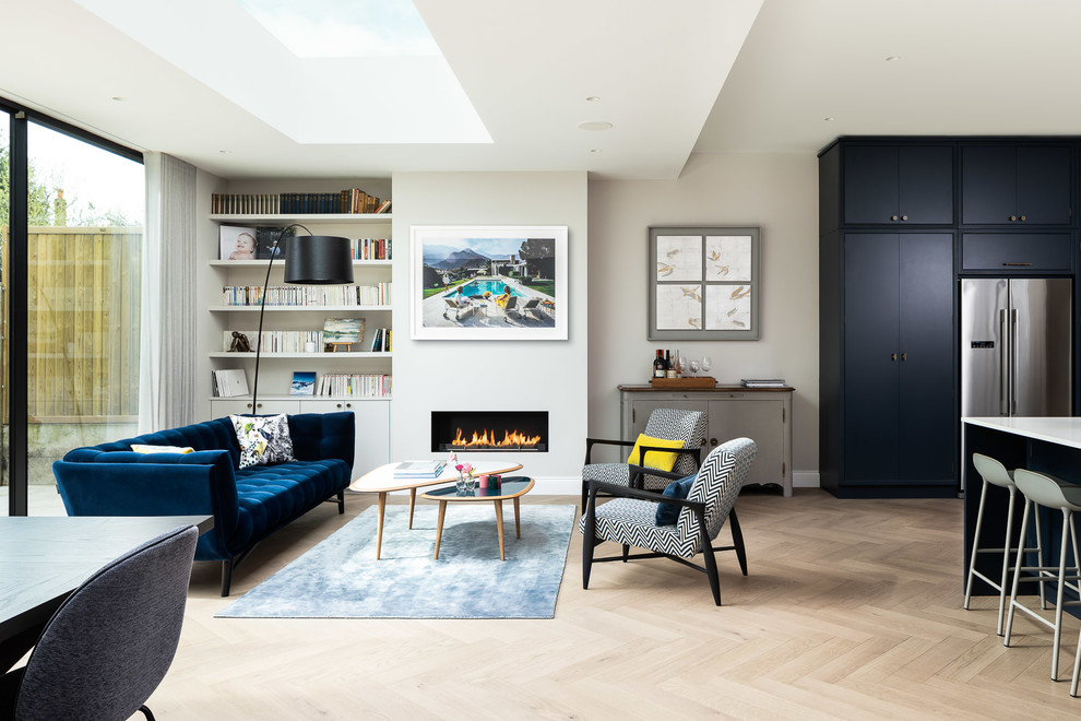 Стильный дизайн: открытая гостиная комната в современном стиле с с книжными шкафами и полками, серыми стенами, светлым паркетным полом, горизонтальным камином, синим диваном и ковром на полу без телевизора - последний тренд