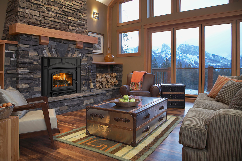 Cette image montre un salon chalet avec un mur marron, un sol en bois brun, un poêle à bois, un manteau de cheminée en pierre et un sol marron.
