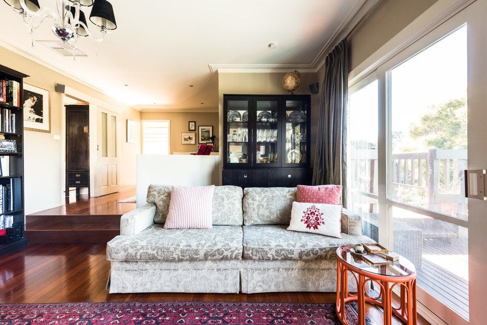 Mittelgroßes, Offenes Eklektisches Wohnzimmer mit beiger Wandfarbe, dunklem Holzboden, Kamin, Kaminumrandung aus Stein, freistehendem TV und rotem Boden in Melbourne