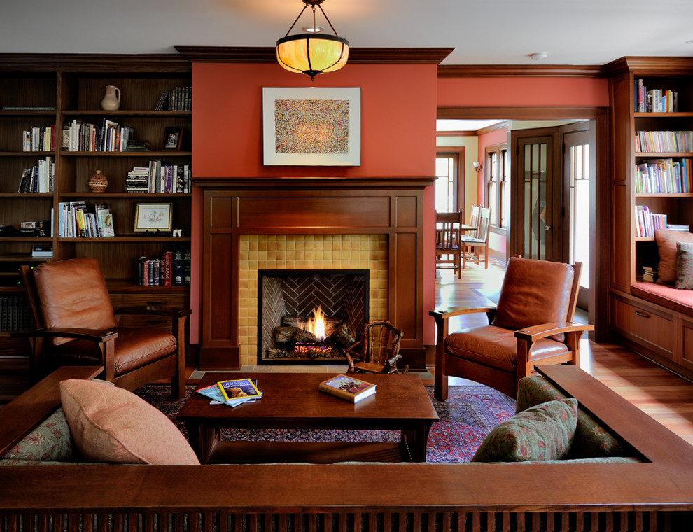 Inspiration för ett amerikanskt separat vardagsrum, med ett bibliotek, röda väggar, mellanmörkt trägolv, en standard öppen spis och en spiselkrans i trä