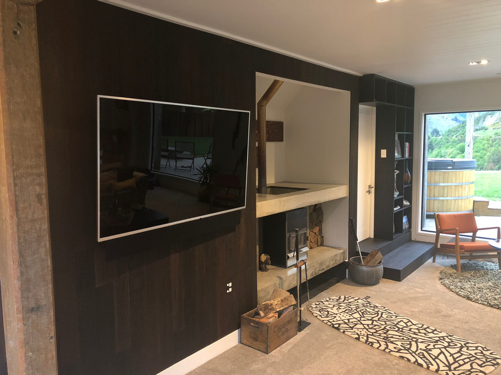 На фото: открытая гостиная комната среднего размера в стиле модернизм с черными стенами, ковровым покрытием, печью-буржуйкой, фасадом камина из бетона и телевизором на стене