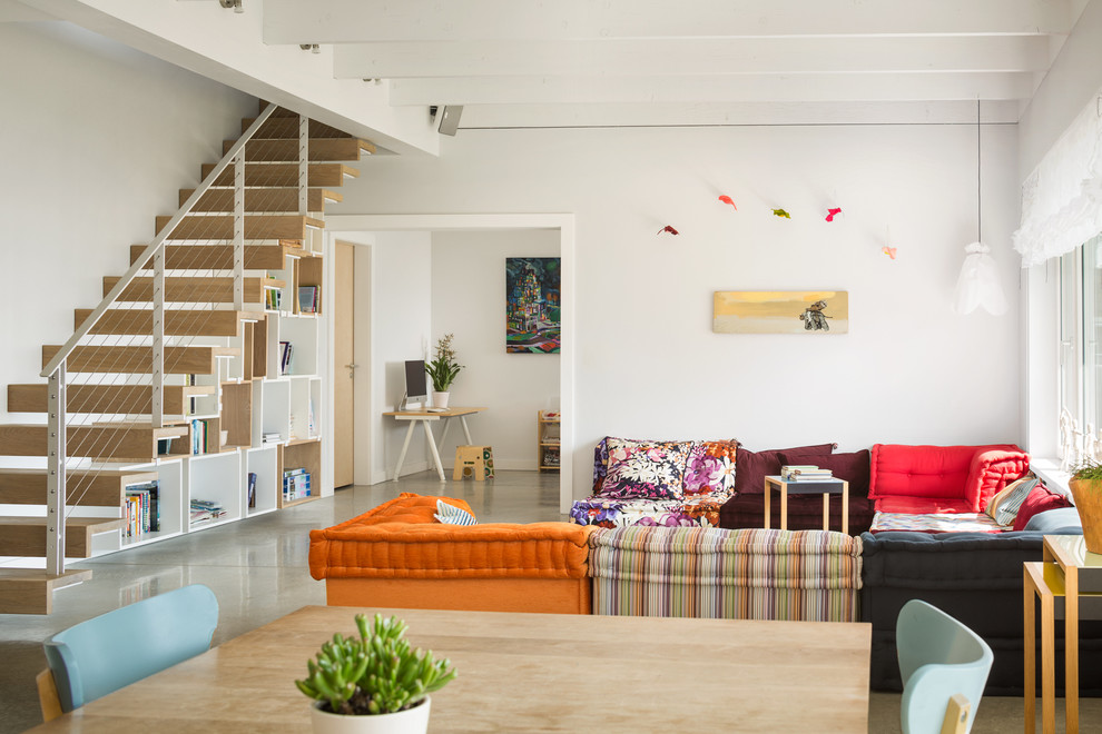 На фото: открытая гостиная комната среднего размера в современном стиле с белыми стенами и бетонным полом без камина с