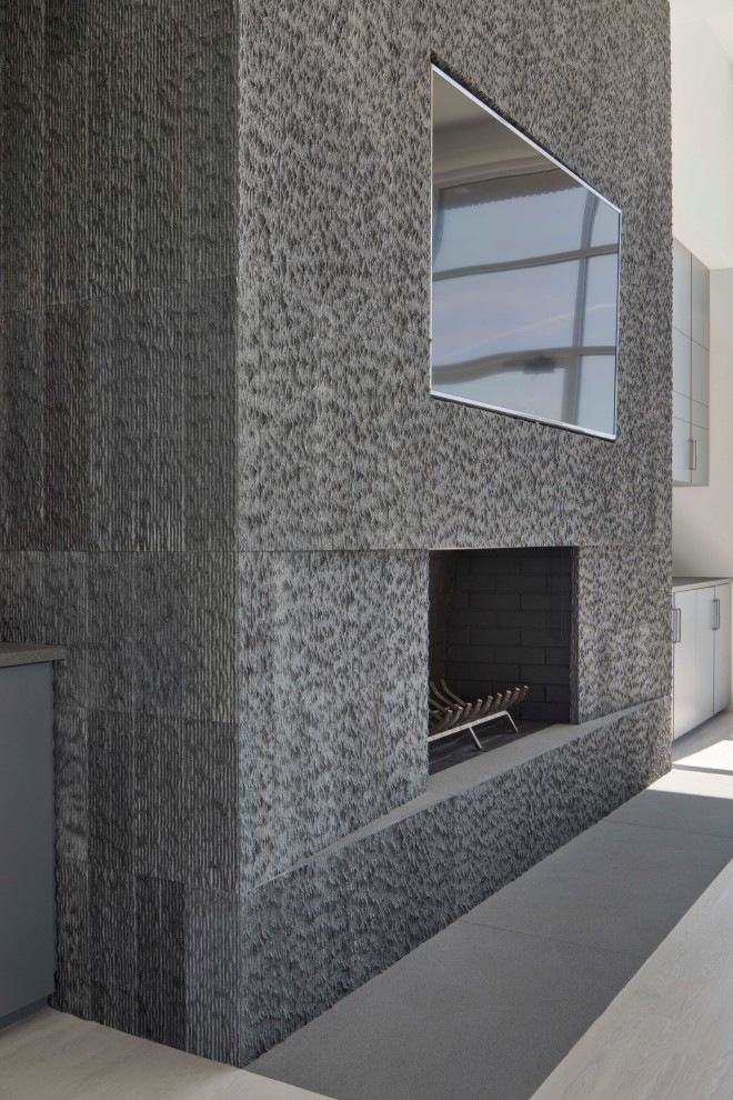 Inspiration pour un grand salon minimaliste ouvert avec un mur gris, parquet clair, une cheminée standard, un manteau de cheminée en pierre, un téléviseur fixé au mur, un sol gris et du lambris.