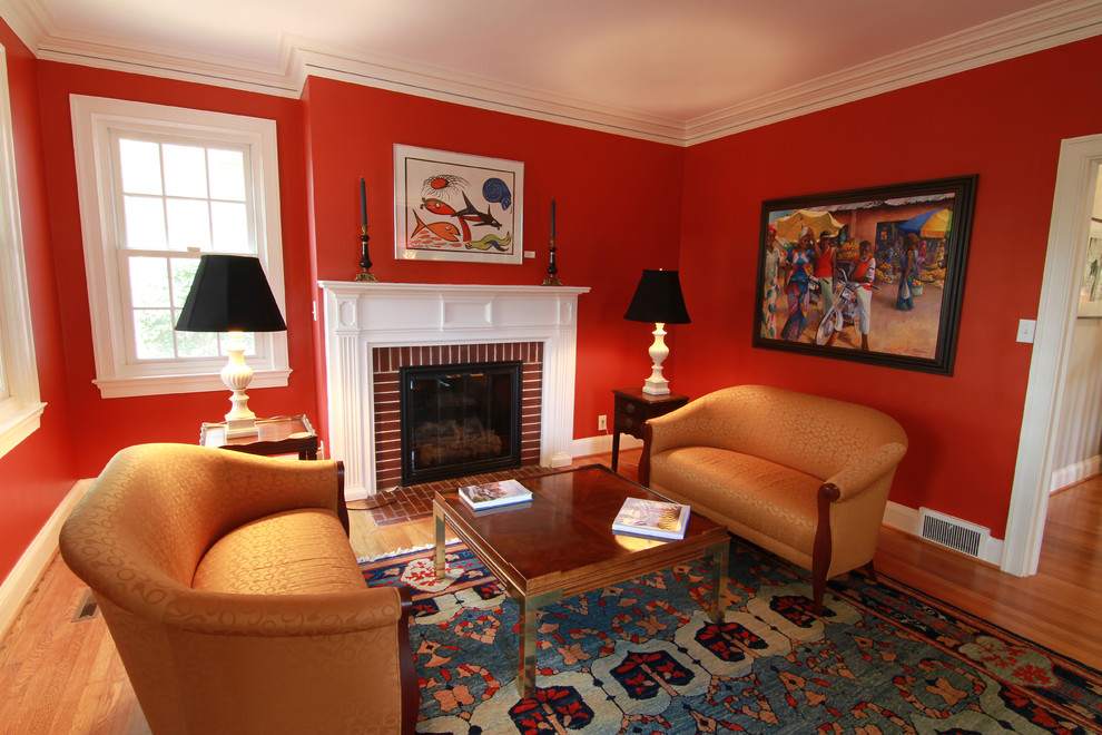Idée de décoration pour un salon tradition de taille moyenne et fermé avec une salle de réception, un mur rouge, un sol en bois brun, une cheminée standard, un manteau de cheminée en brique et aucun téléviseur.