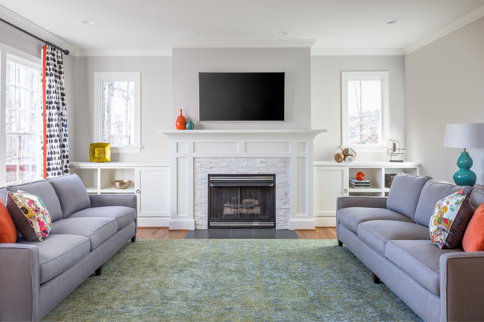 ローリーにある高級な広いトランジショナルスタイルのおしゃれなリビング (グレーの壁、無垢フローリング、標準型暖炉、石材の暖炉まわり、壁掛け型テレビ、茶色い床) の写真