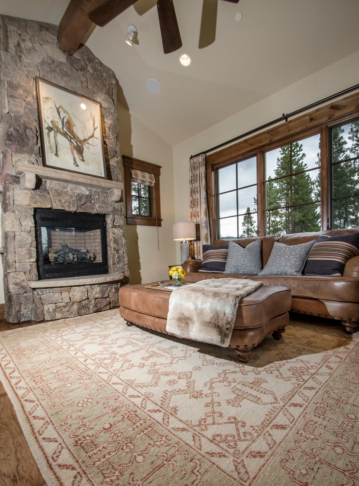 Inspiration for a mid-sized rustic enclosed light wood floor living room remodel in Denver with beige walls, a standard fireplace, a stone fireplace and a concealed tv