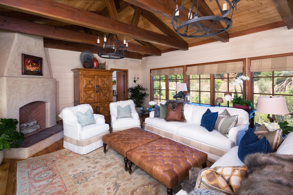 Cette photo montre un salon sud-ouest américain de taille moyenne et ouvert avec une salle de réception, un mur beige, un sol en bois brun, une cheminée d'angle, un manteau de cheminée en plâtre et un téléviseur dissimulé.