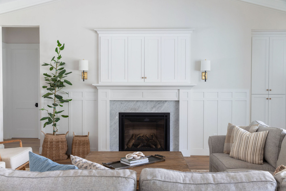 Cette image montre un grand salon traditionnel ouvert avec un mur blanc, un sol en bois brun, une cheminée standard, un manteau de cheminée en bois, un téléviseur encastré, un sol marron, un plafond voûté et boiseries.