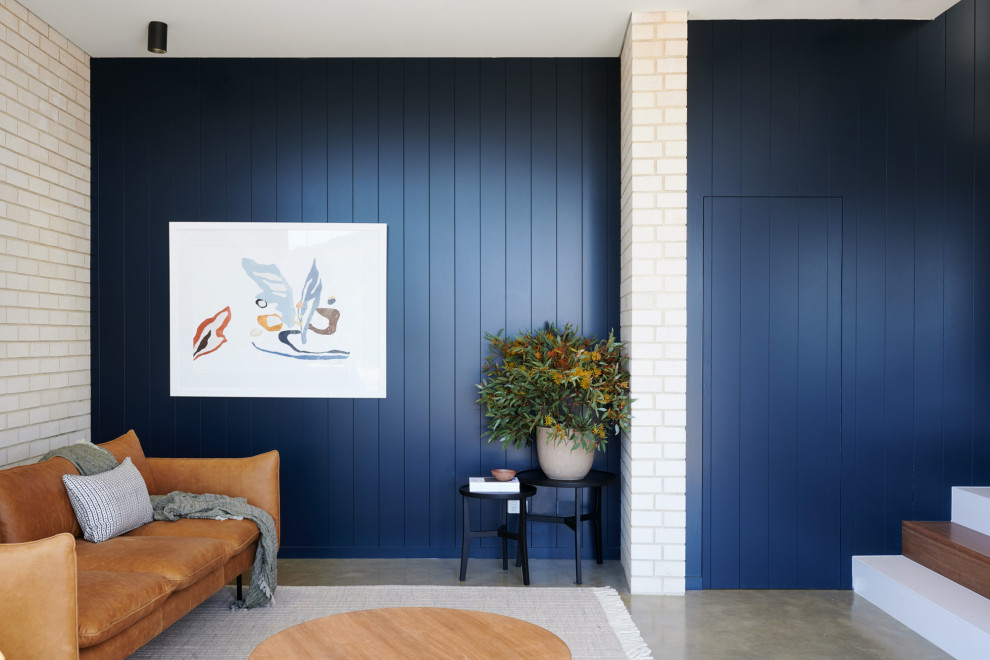 Foto de salón abierto de tamaño medio con paredes azules, suelo de cemento, televisor colgado en la pared y suelo gris