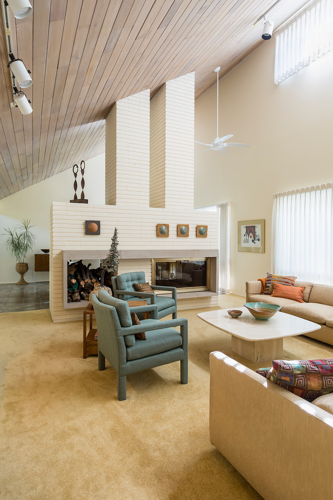 Ejemplo de salón para visitas abierto retro grande con paredes blancas, moqueta, chimenea de doble cara, marco de chimenea de ladrillo y suelo beige