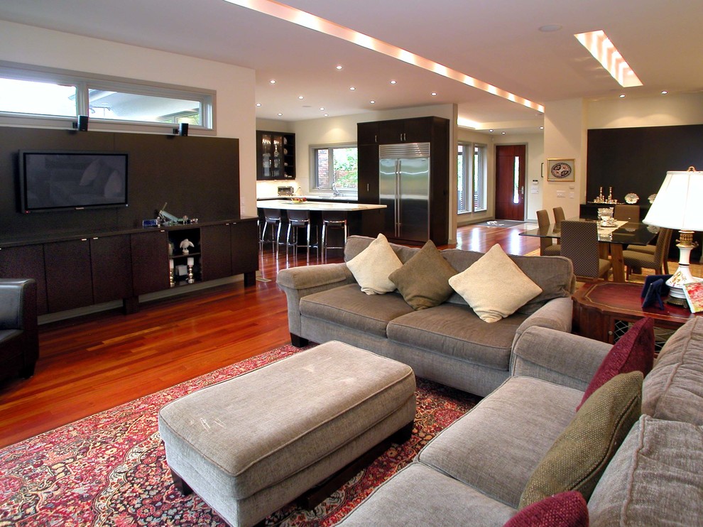 Пример оригинального дизайна: большая открытая гостиная комната в современном стиле с бежевыми стенами, паркетным полом среднего тона, телевизором на стене и коричневым полом