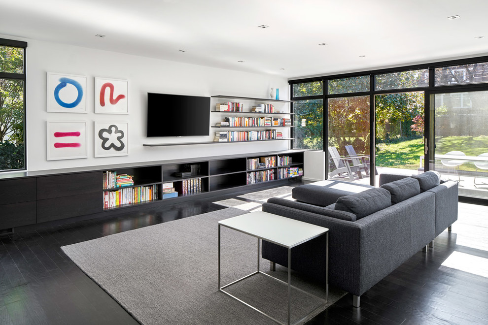 Diseño de biblioteca en casa abierta contemporánea sin chimenea con paredes blancas, suelo de madera oscura, televisor colgado en la pared y alfombra