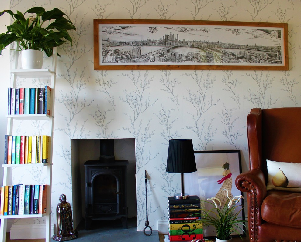 Imagen de biblioteca en casa abierta ecléctica pequeña sin televisor con paredes grises, suelo de madera clara, estufa de leña y marco de chimenea de hormigón