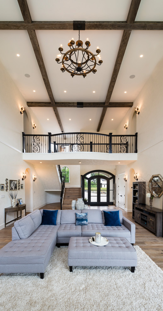 Inspiration for a large mediterranean open plan living room in Vancouver with white walls, medium hardwood flooring, a standard fireplace, a brick fireplace surround, a wall mounted tv and brown floors.