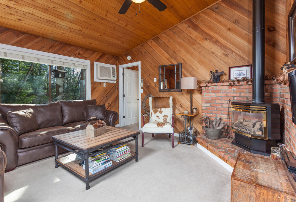 Esempio di un piccolo soggiorno stile rurale chiuso con pareti marroni, moquette, stufa a legna e TV a parete