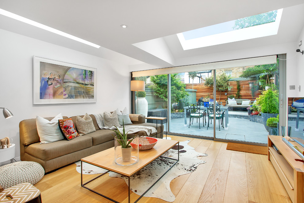 This is an example of a medium sized contemporary enclosed living room in London with white walls, light hardwood flooring, a freestanding tv and beige floors.