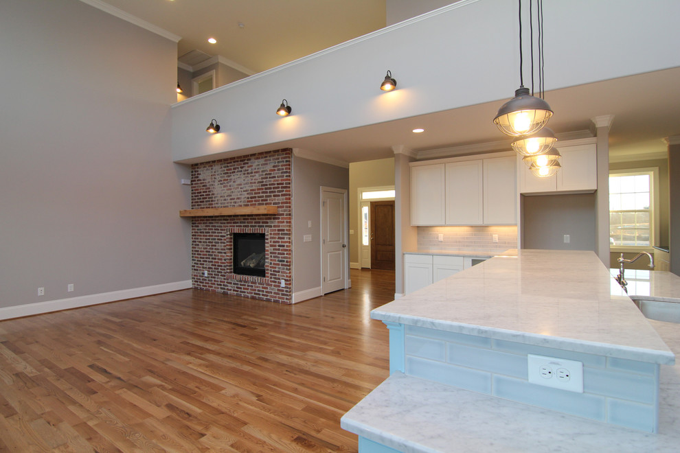 Photo of a large contemporary open plan living room in Raleigh with grey walls, light hardwood flooring, a standard fireplace and a brick fireplace surround.