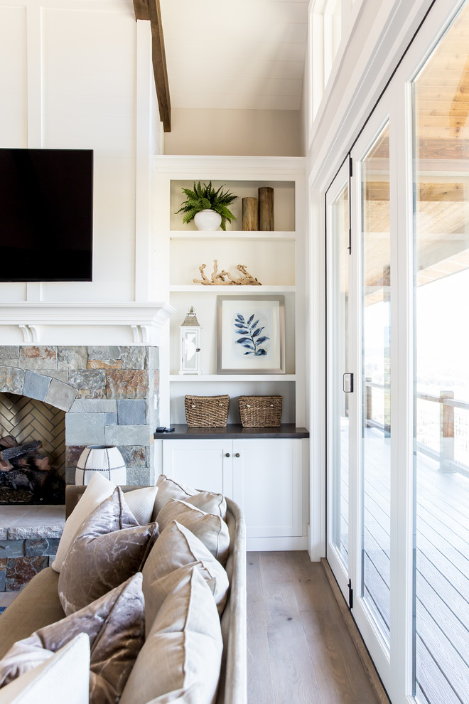 Cette photo montre un grand salon nature ouvert avec un mur blanc, un sol en bois brun, une cheminée standard, un manteau de cheminée en pierre et un téléviseur fixé au mur.