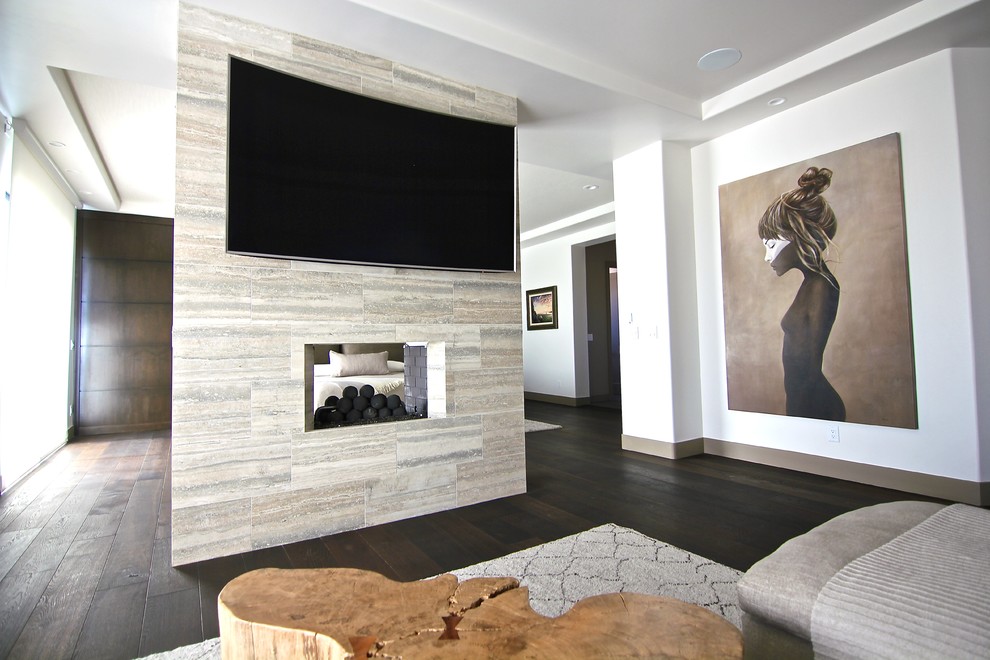 Стильный дизайн: огромная изолированная гостиная комната в стиле модернизм с белыми стенами, полом из керамогранита, двусторонним камином, фасадом камина из плитки и телевизором на стене - последний тренд