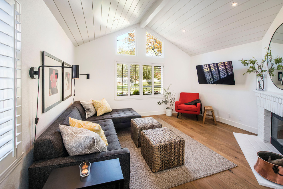 Example of a trendy medium tone wood floor and shiplap ceiling living room design in San Francisco with white walls, a corner fireplace, a brick fireplace and a wall-mounted tv