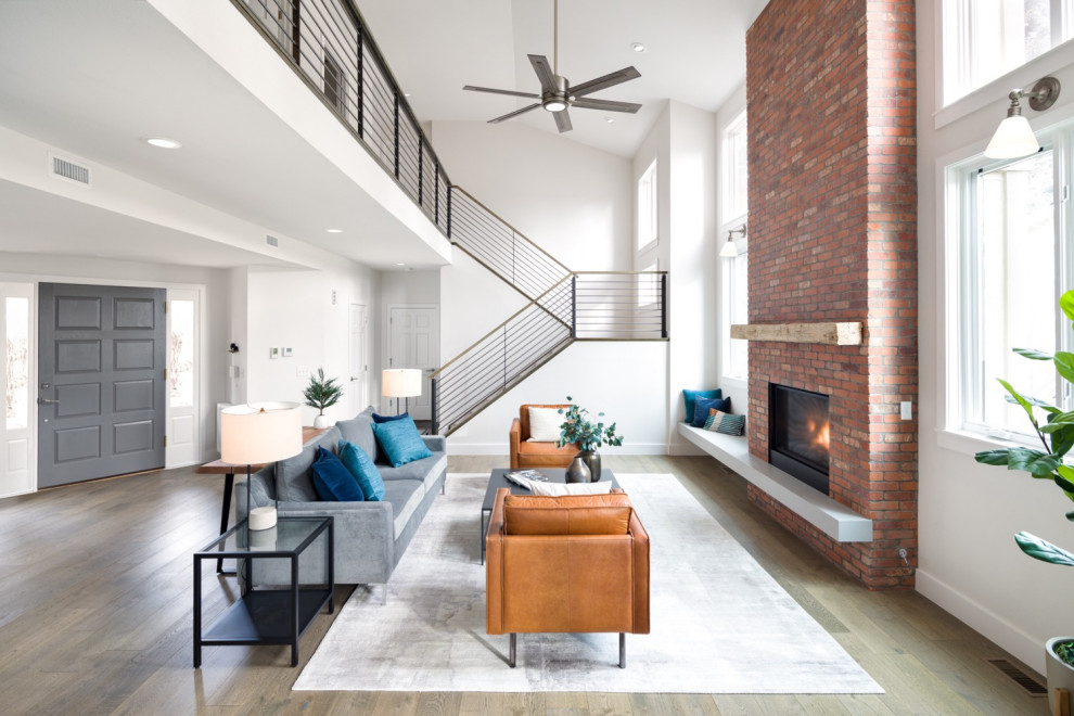 Large industrial open plan living room in Denver with white walls, medium hardwood flooring, a standard fireplace, a brick fireplace surround, no tv and brown floors.
