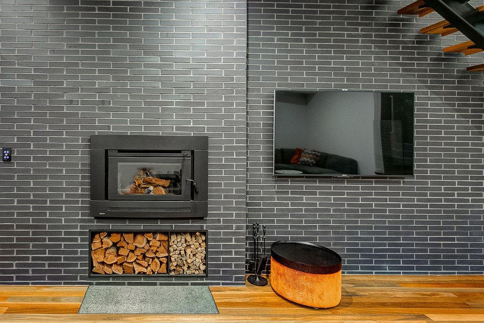 Imagen de salón abierto actual de tamaño medio con suelo de madera en tonos medios, marco de chimenea de ladrillo y televisor colgado en la pared