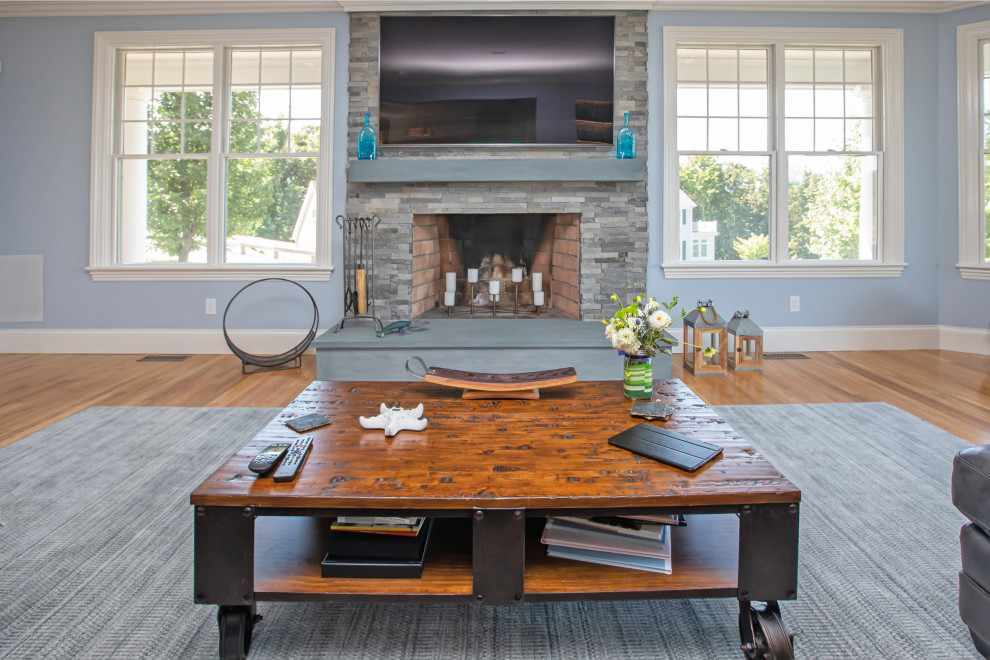 Cette image montre un grand salon minimaliste fermé avec un bar de salon, un mur gris, un sol en bois brun, une cheminée standard, un manteau de cheminée en pierre de parement, un téléviseur fixé au mur et un sol marron.
