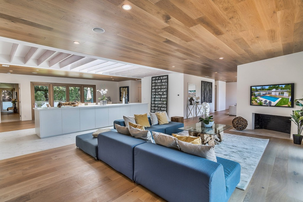 Large retro open plan living room in Los Angeles with white walls, light hardwood flooring, a standard fireplace, a wall mounted tv and brown floors.