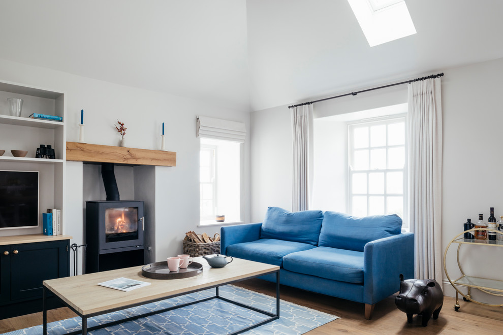 Mittelgroßes, Offenes Maritimes Wohnzimmer mit weißer Wandfarbe, braunem Holzboden, Kaminofen und braunem Boden in Cornwall