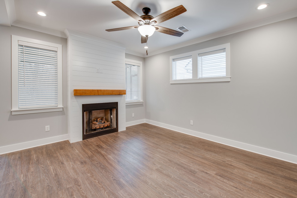 Cette image montre un grand salon craftsman ouvert avec une salle de réception, un mur gris, un sol en vinyl, une cheminée standard, un manteau de cheminée en bois, aucun téléviseur et un sol marron.