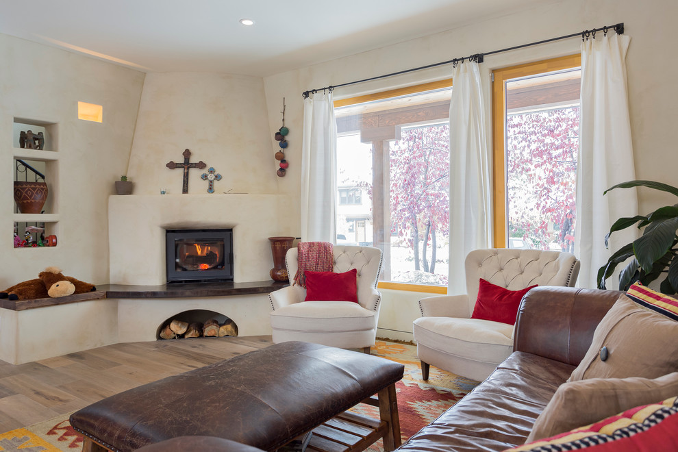 Foto de salón abierto de estilo americano de tamaño medio con paredes beige, suelo de madera clara, estufa de leña, marco de chimenea de yeso y suelo beige