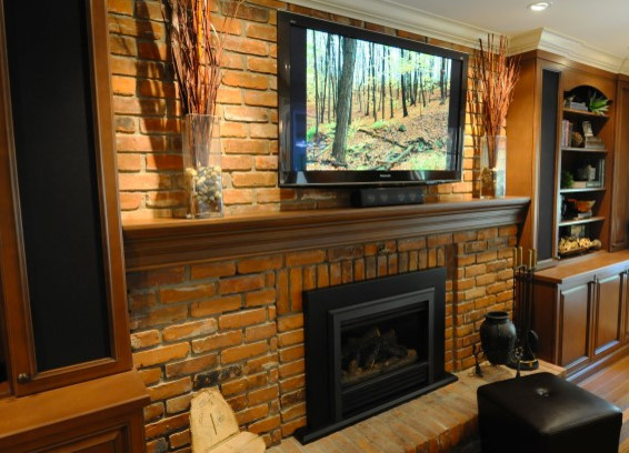 Cette photo montre un salon chic avec un téléviseur fixé au mur, une cheminée standard, un manteau de cheminée en brique et un sol en bois brun.