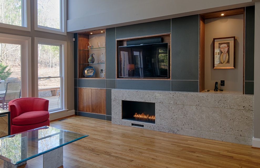 Diseño de salón abierto moderno con paredes grises, suelo de madera clara, chimenea lineal, marco de chimenea de piedra y pared multimedia