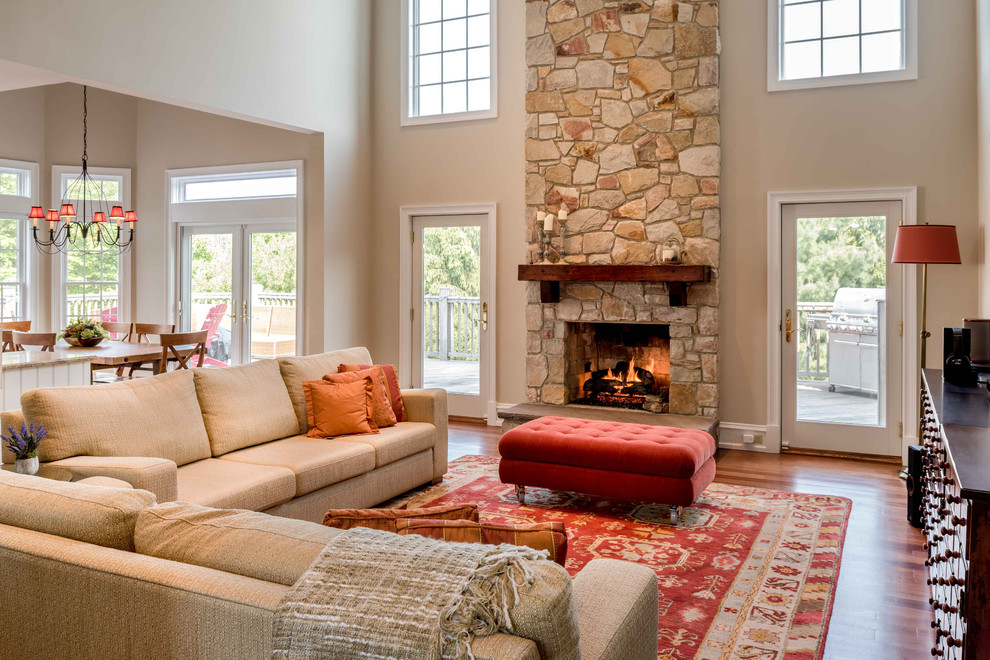 Aménagement d'un salon classique ouvert avec un mur beige, un sol en bois brun, une cheminée standard et un manteau de cheminée en pierre.