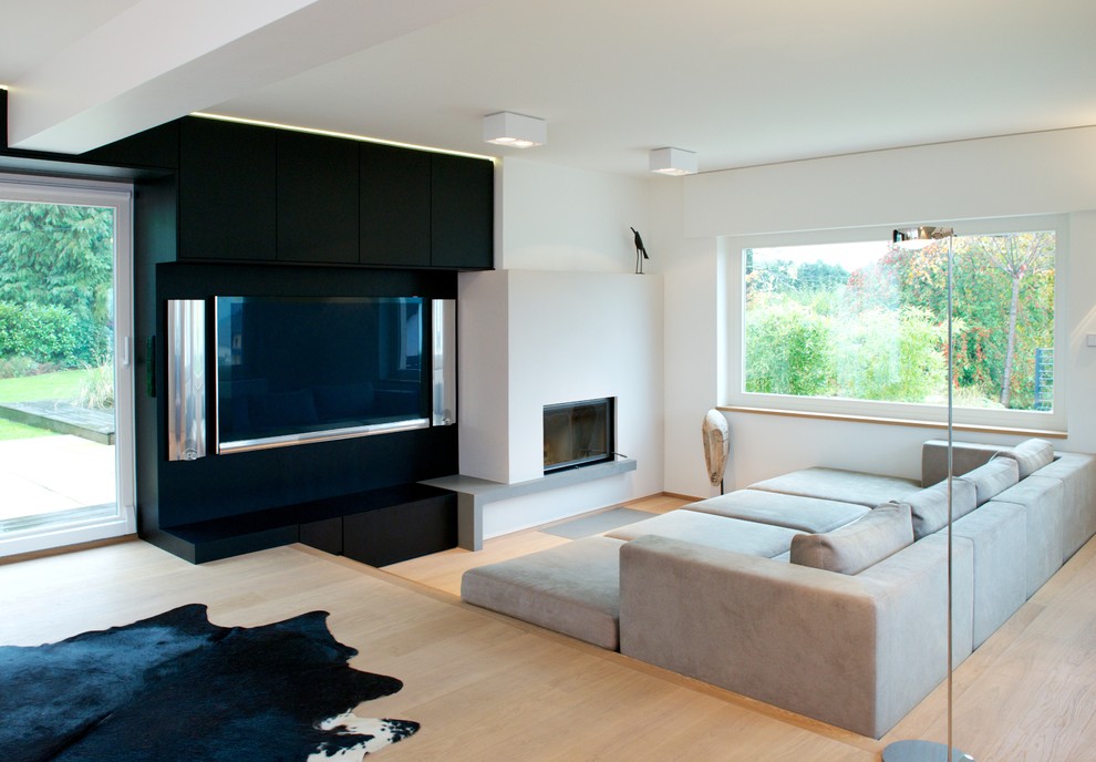 Modelo de salón abierto moderno de tamaño medio con paredes blancas, suelo de madera clara y pared multimedia