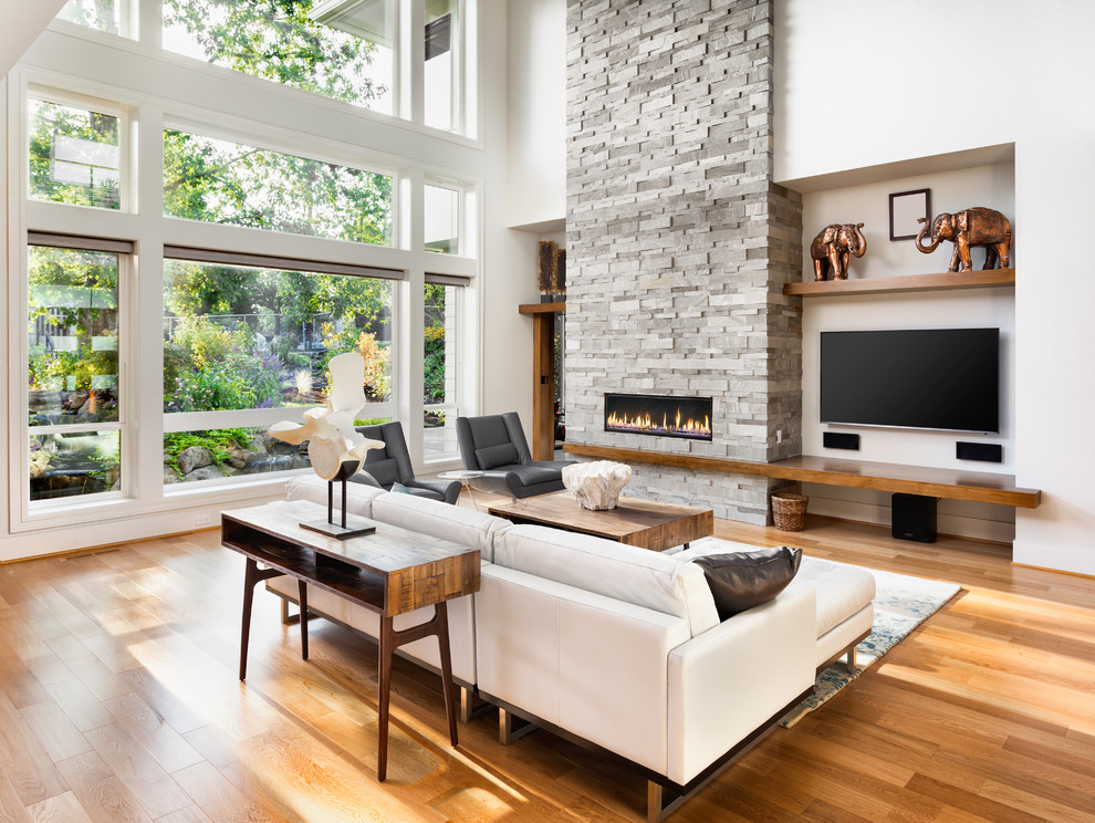 Modernes Wohnzimmer mit weißer Wandfarbe, braunem Holzboden, Gaskamin, Kaminumrandung aus Stein, TV-Wand und braunem Boden in Los Angeles