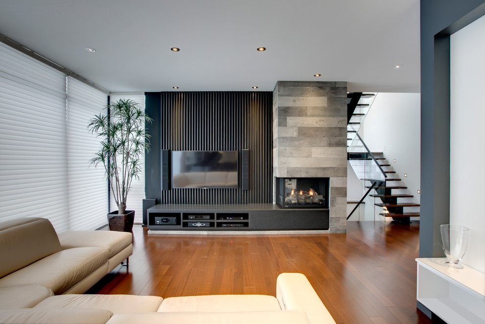 Ejemplo de salón actual con suelo de madera en tonos medios, chimenea de esquina, marco de chimenea de hormigón y televisor colgado en la pared
