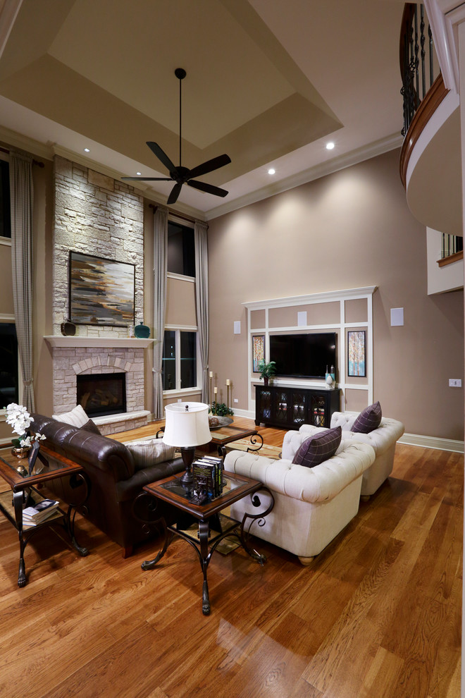 Cette photo montre un grand salon chic ouvert avec un mur beige, un sol en bois brun, une cheminée standard, un manteau de cheminée en brique et un téléviseur fixé au mur.
