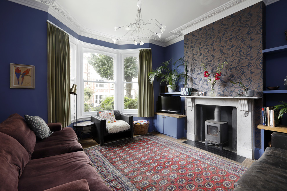 サセックスにある中くらいなエクレクティックスタイルのおしゃれなリビング (青い壁、無垢フローリング、薪ストーブ、石材の暖炉まわり、据え置き型テレビ、マルチカラーの床) の写真