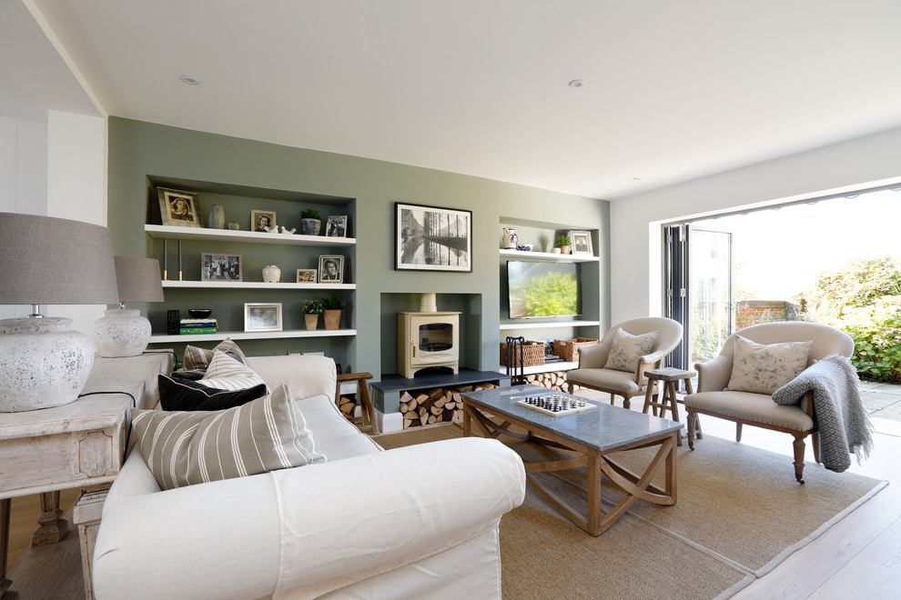 Medium sized classic formal open plan living room in Sussex with light hardwood flooring, a wood burning stove, a plastered fireplace surround, beige floors, green walls and a wall mounted tv.