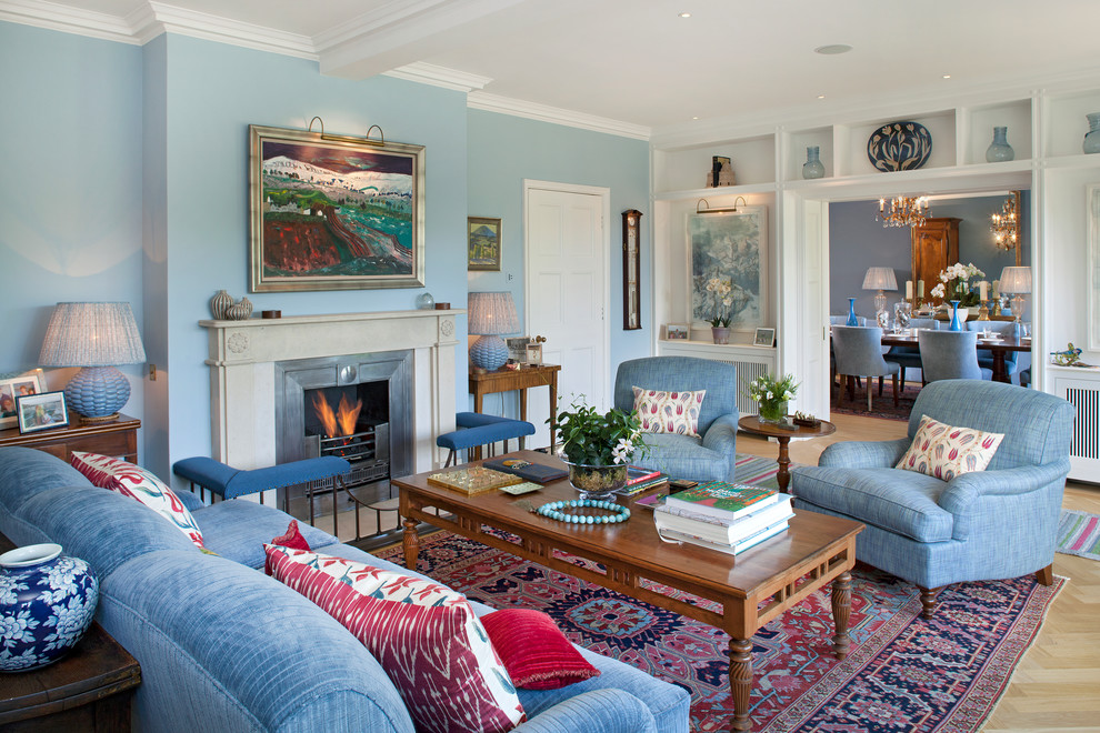 На фото: гостиная комната в классическом стиле с синими стенами, светлым паркетным полом, стандартным камином и синим диваном без телевизора