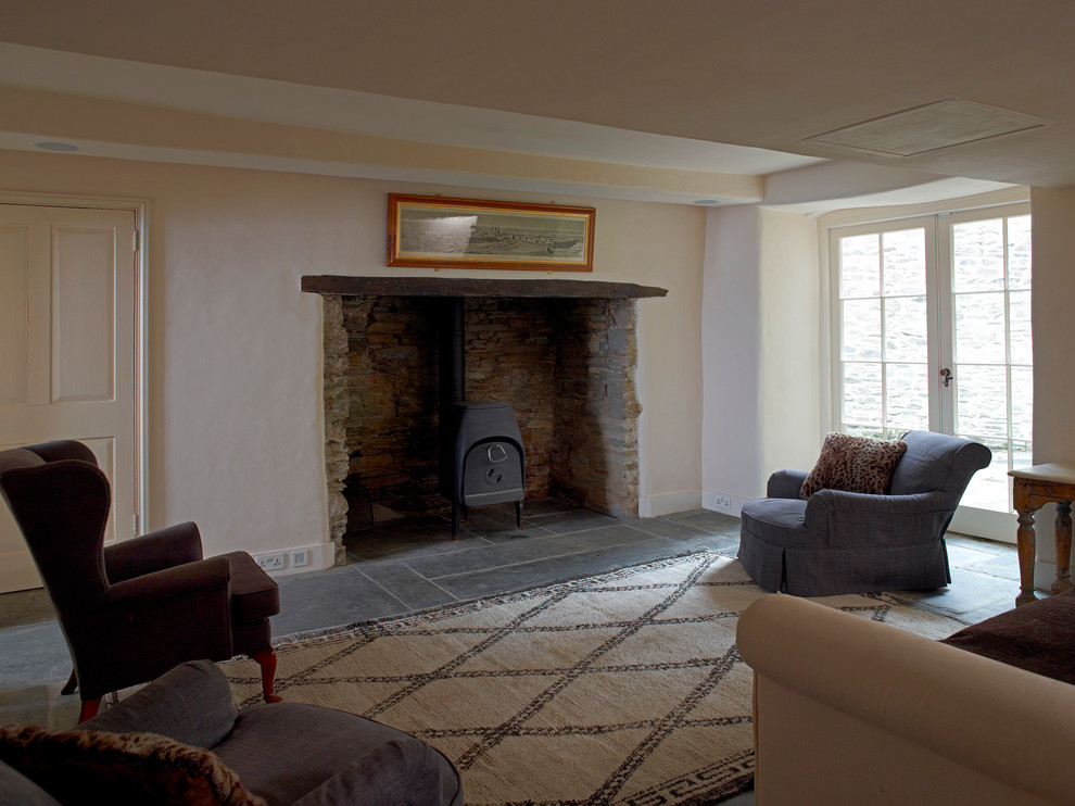 Aménagement d'un salon classique de taille moyenne et fermé avec un mur beige, un sol en ardoise, un poêle à bois et un manteau de cheminée en pierre.