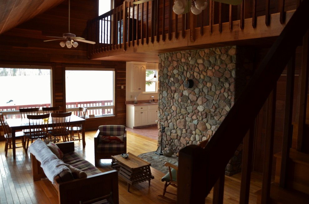 Foto de salón abierto marinero grande con paredes marrones, suelo de madera clara, estufa de leña y marco de chimenea de piedra