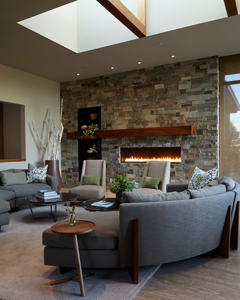 Cette image montre un grand salon design ouvert avec un mur beige, parquet clair, une cheminée standard, un manteau de cheminée en pierre, un téléviseur fixé au mur et un sol gris.